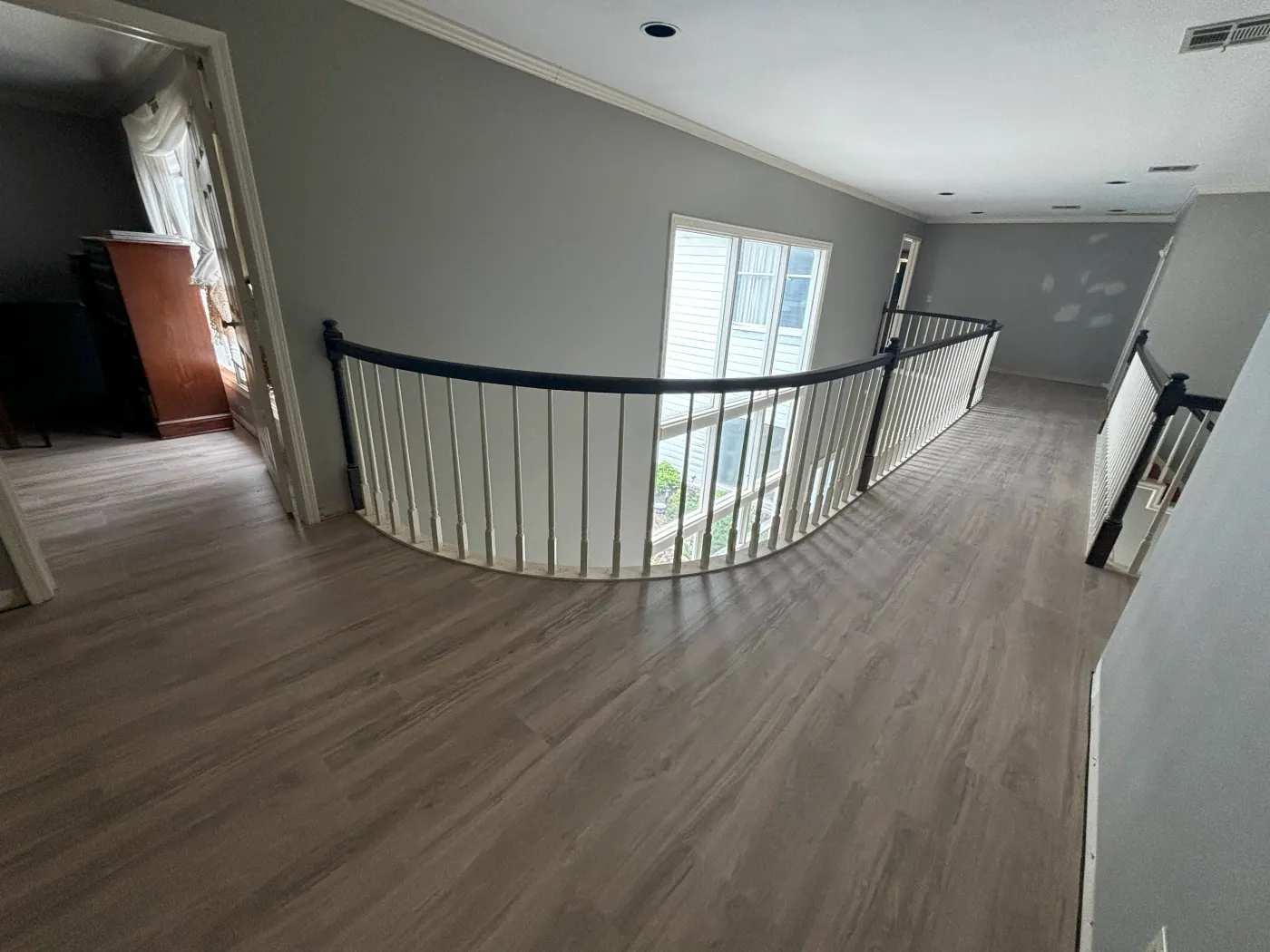 Gray plank flooring on a curved upstairs landing with iron railing in a Tulsa, OK home